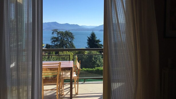 Ein Balkon mit Tisch und Stühlen mit Blick auf ein Gewässer und Berge.