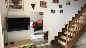 Ein Wohnzimmer mit Fernseher, einer Holztreppe, einem Spiegel und einer Wand mit Fotos.