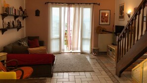 Ein gemütliches Wohnzimmer mit einer Couch, einem Couchtisch und einem Bücherregal. Eine Treppe führt auf eine obere Ebene.