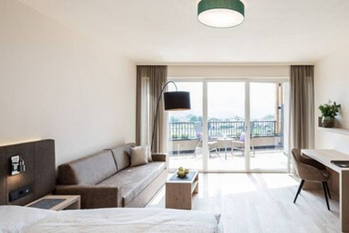Una habitación de hotel moderna con una cama, un sofá, un escritorio y un balcón con vistas.