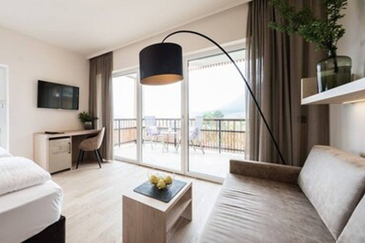 Habitación de hotel con cama, escritorio, sofá, televisor y balcón con vistas.