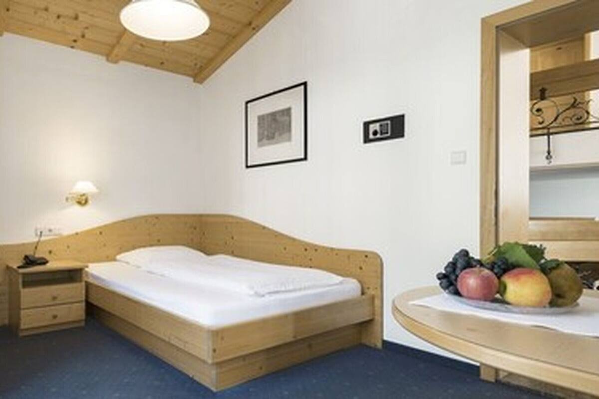 Una cama de madera en una habitación con una mesita de noche pequeña, una lámpara de pared y un cuadro enmarcado.