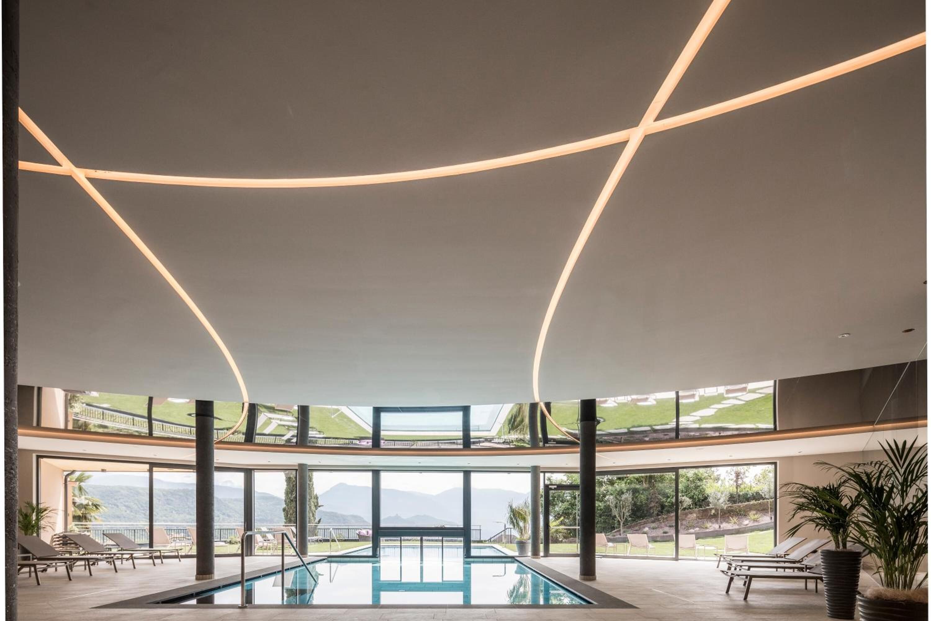 Ein moderner, überdachter Pool mit Blick auf Berge und einer Liegewiesen mit Liegestühlen.