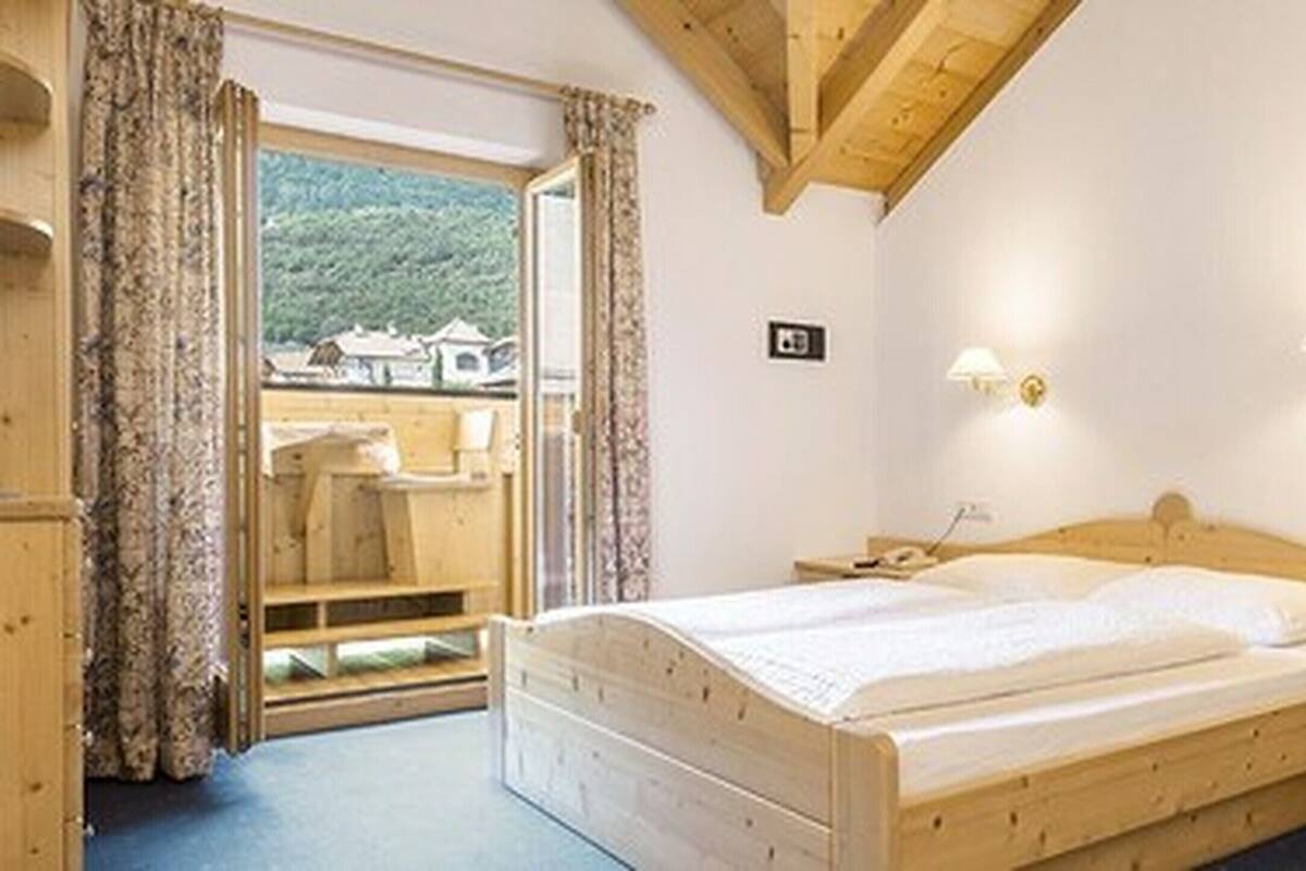Una cama de madera en una habitación con vistas a un paisaje montañoso. Hay dos mesitas de noche con lámparas.