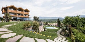 A two-story building with balconies, a swimming pool, and a well-maintained lawn with stone pathways. - Hotel Torgglhof Kaltern (Caldaro Sulla Strada del Vino)