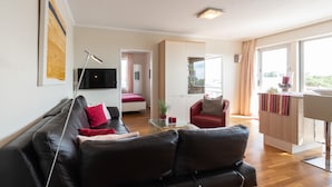 A modern living room with a leather sofa, a glass coffee table, and a red armchair. There is a flat-screen TV mounted on the wall and a large window providing natural light. - Wonderful view for 4 people 100 m from the main beach (Wangerooge)