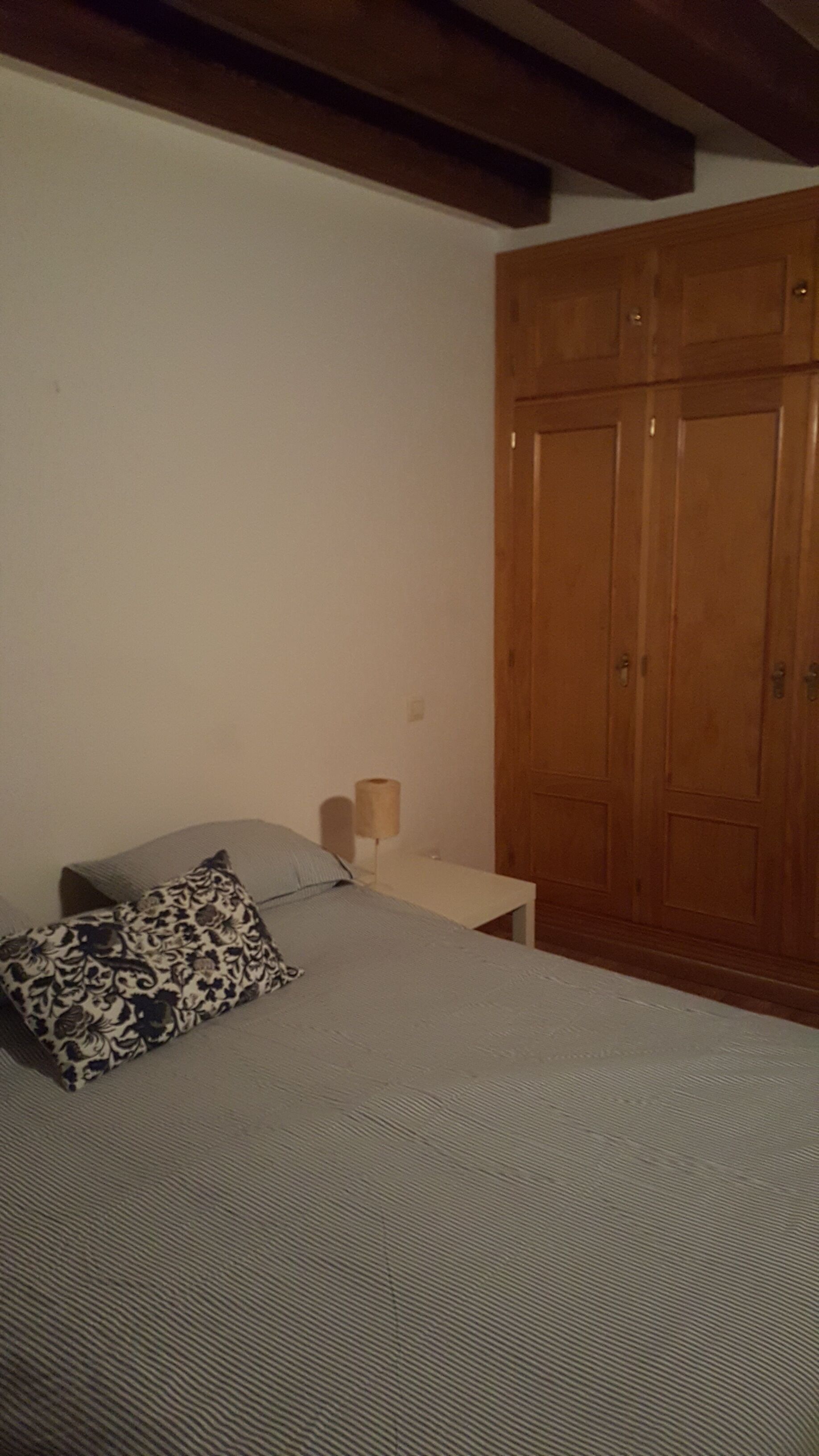 Un dormitorio con cama, mesita de noche, lámpara y armario de madera.