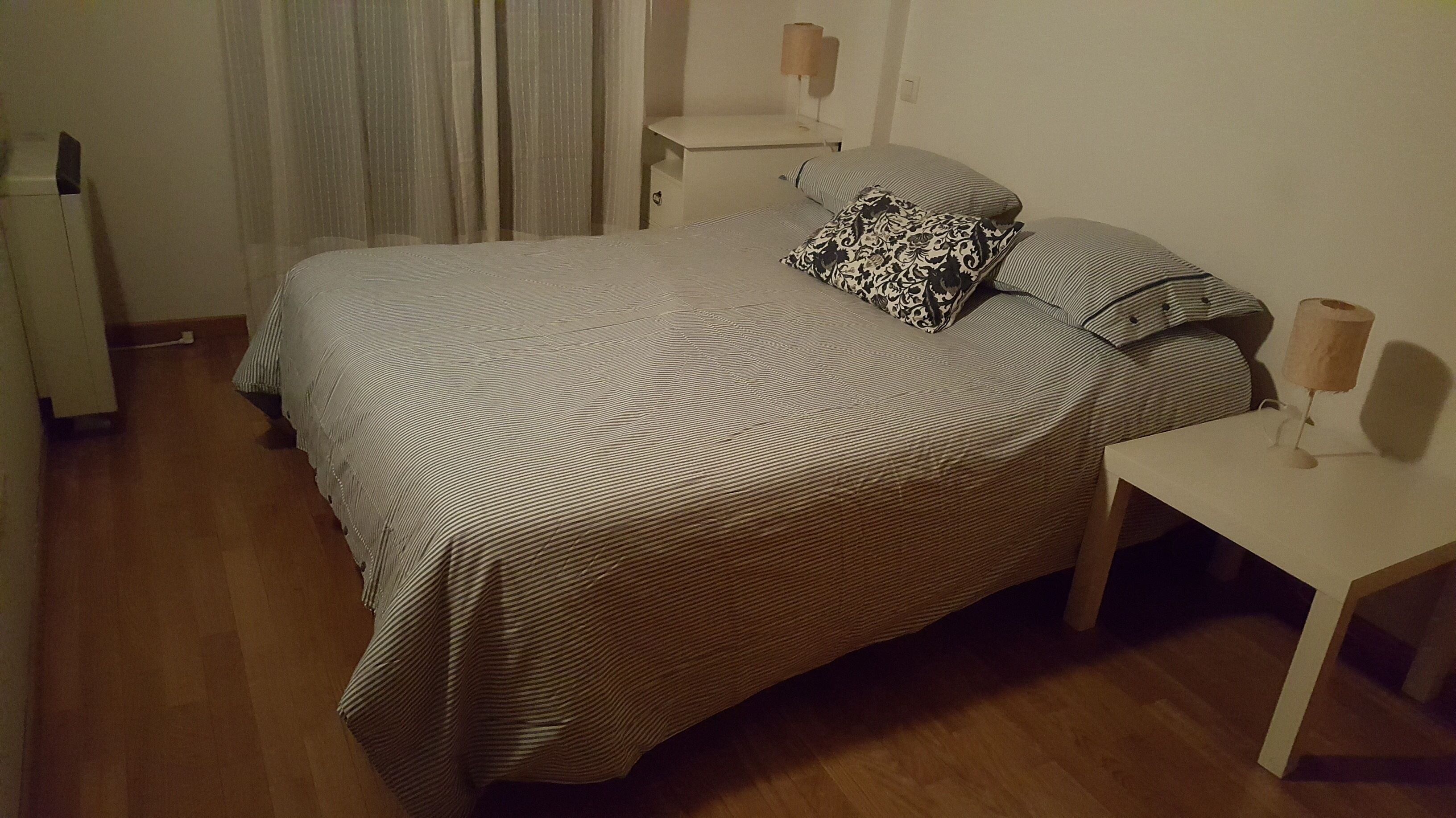 Un dormitorio con una cama grande, dos mesitas de noche, una lámpara en cada mesita y una cortina.