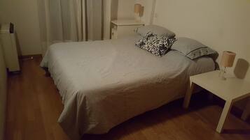 Un dormitorio con una cama grande, dos mesitas de noche, una lámpara en cada mesita y una cortina.