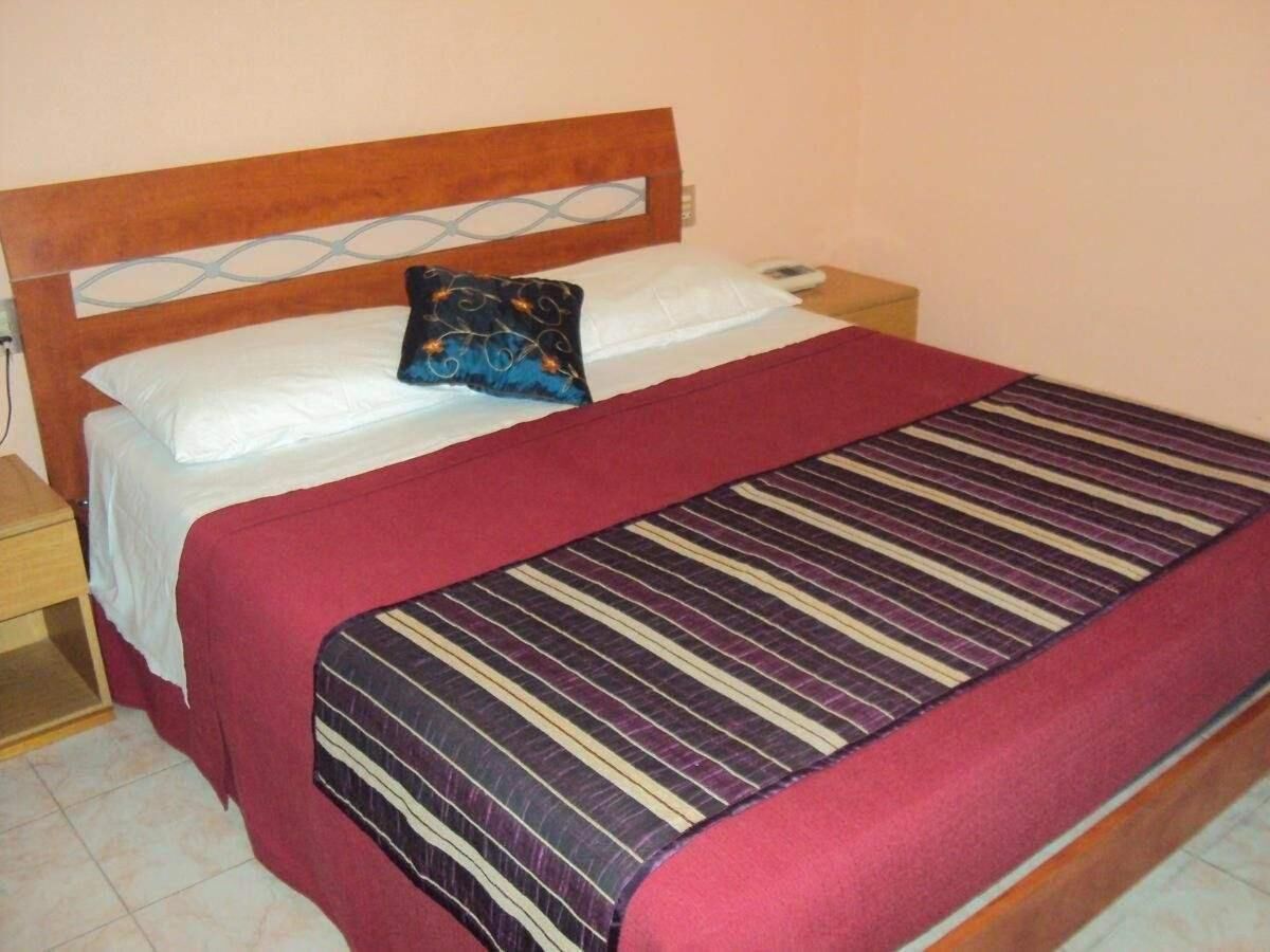 Un letto singolo con testiera in legno, cuscini bianchi e copripiumone a righe rosse e viola.