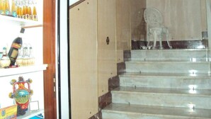 A staircase with a chair at the top, leading to a room with a wooden door and a shelf with bottles and a decorative item. - Hotel Mirage (Messina)