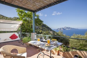 Terraço com mesa posta para o pequeno-almoço, com vista para a paisagem costeira.