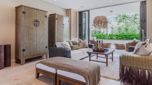 Un salon moderne avec un canapé, un banc et un grand meuble. Une fenêtre offre une vue sur la verdure à l’extérieur.