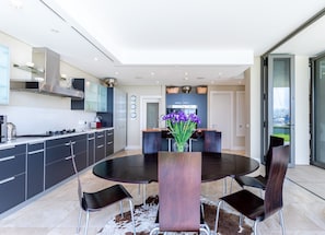 A modern kitchen with a dining area, featuring a round table with chairs, a coffee machine, and a vase with purple flowers. - 005 Palgrave on the Waterfront Marina (Cape Town)