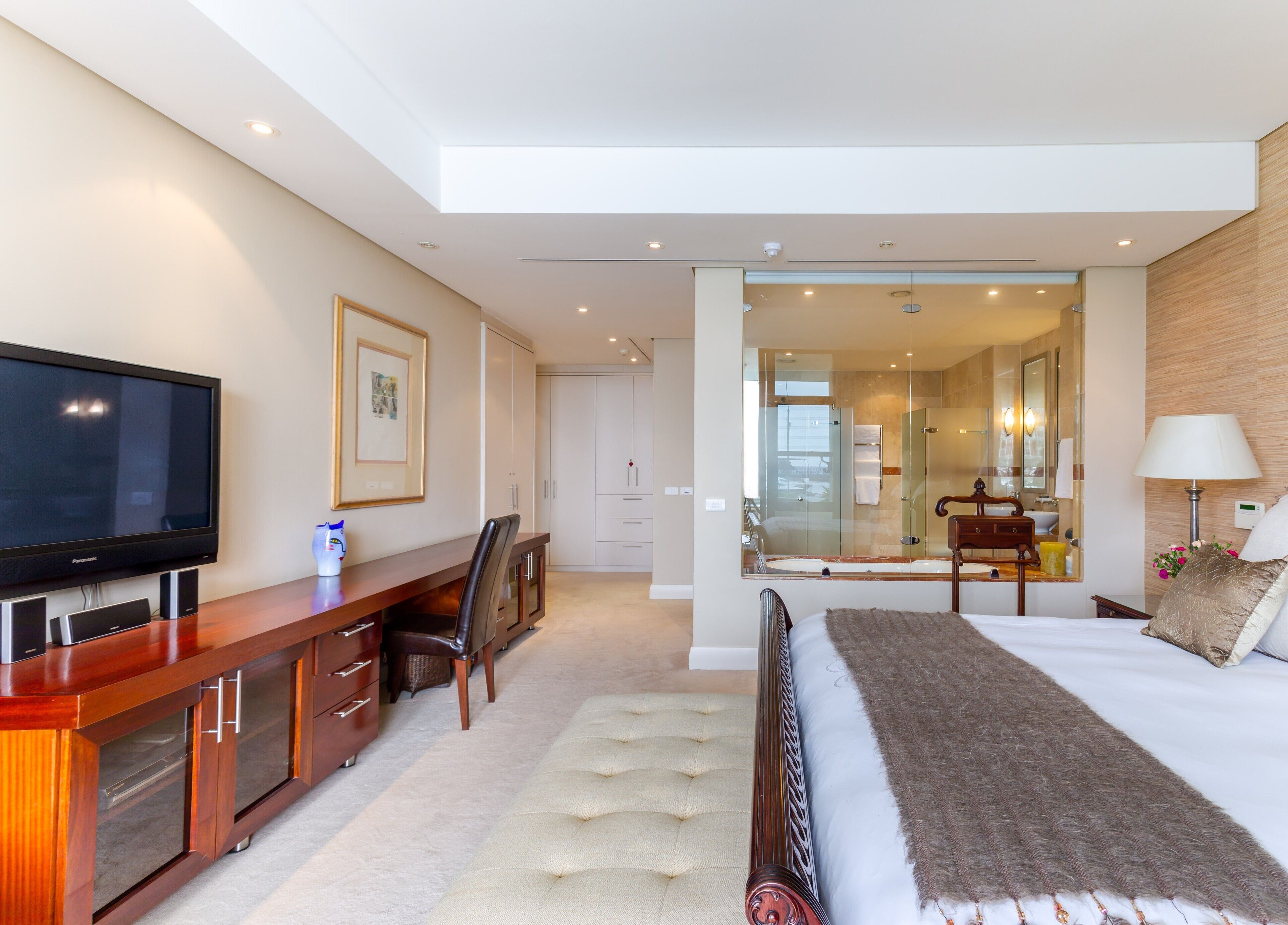 A modern hotel room with a flat-screen TV, a desk with a chair, a bed with a large pillow, and a walk-in closet.