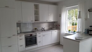 A modern kitchen with white cabinetry, a built-in oven, and a window with curtains. - **** NEW **** Ferienhaus Meerzeit Eckernförde **** NEW ****  (Eckernförde)