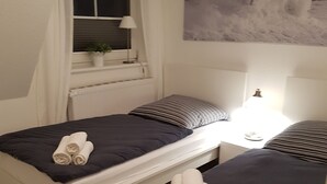 A bedroom with two beds, a window with curtains, a radiator, a potted plant, and a painting of a snowy landscape. - **** NEW **** Ferienhaus Meerzeit Eckernförde **** NEW ****  (Eckernförde)