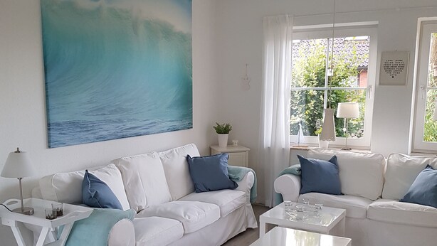 A living room with two white sofas, a coffee table, and a painting of the ocean. - **** NEW **** Ferienhaus Meerzeit Eckernförde **** NEW ****  (Eckernförde)