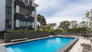 A modern building with a swimming pool, outdoor seating, and a view of trees. - 202 Warwick (Cape Town)