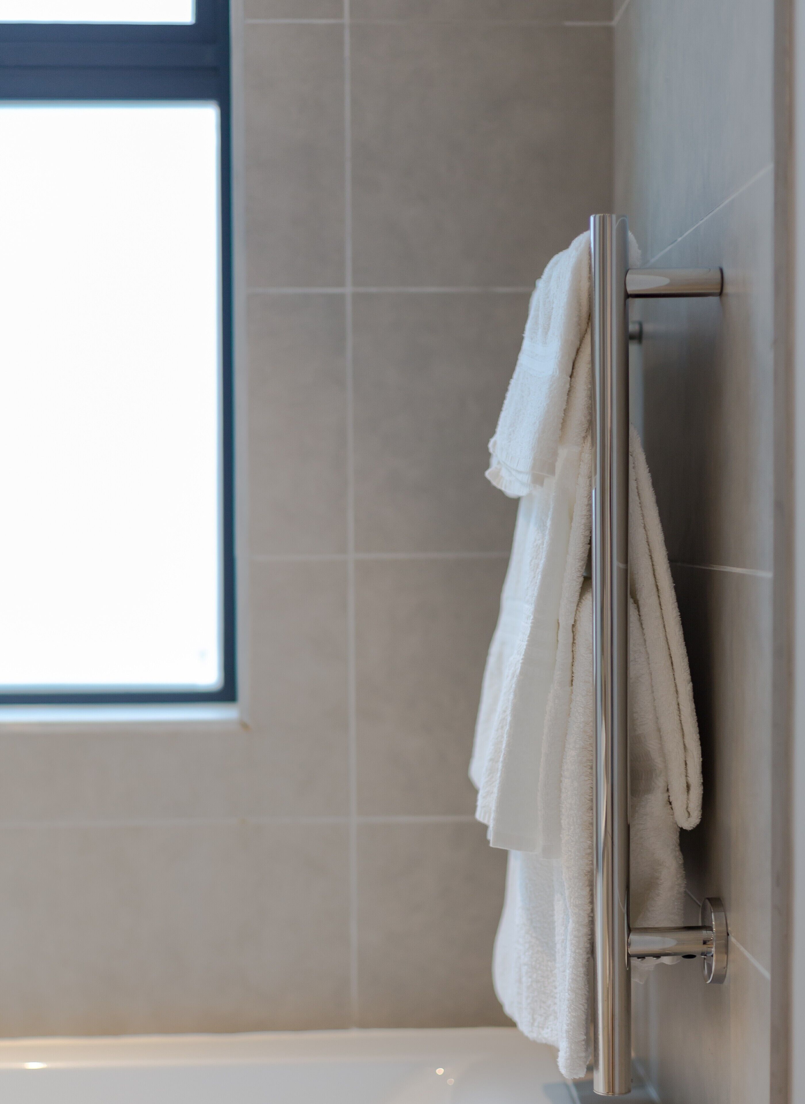 Un baño con una bañera, un perchero con dos toallas y una ventana.