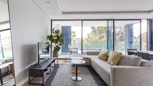 Uma sala de estar moderna com sofá, mesa de centro, TV e uma grande janela com vista para o exterior.