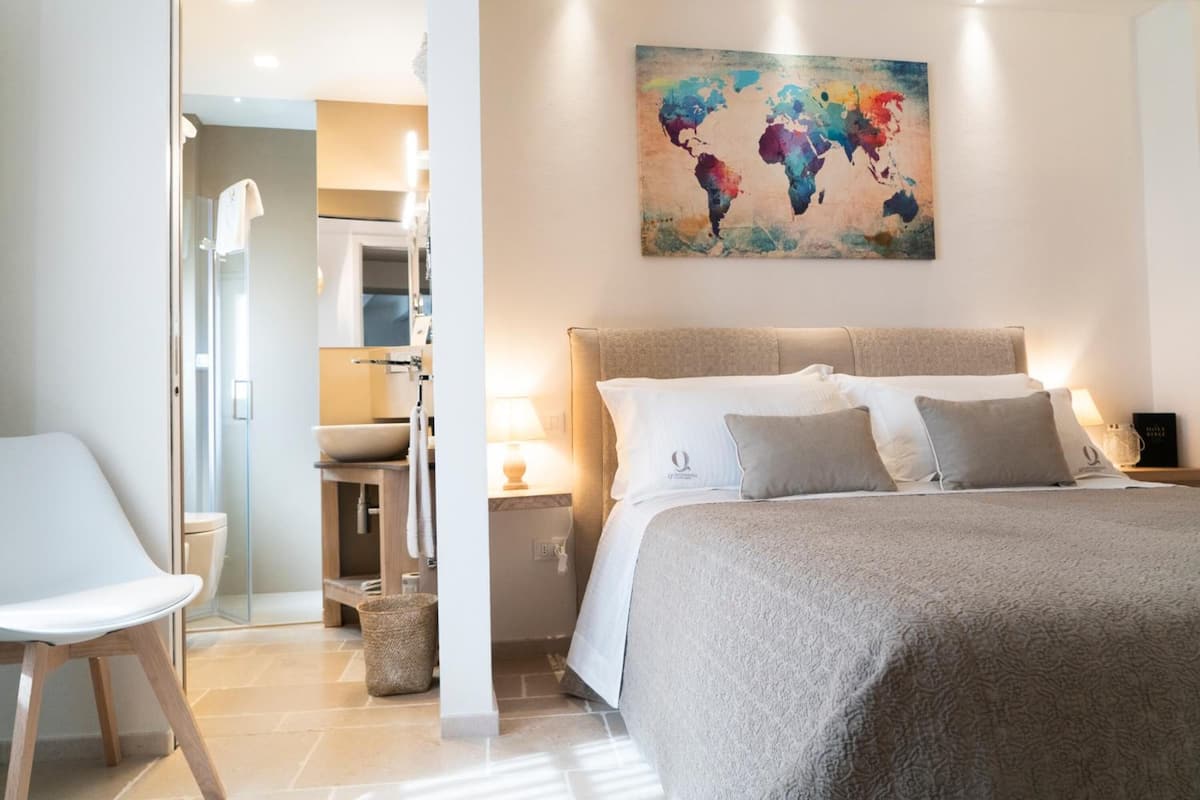 Een slaapkamer met een groot bed, een nachtkastje met een lamp, een wereldkaart aan de muur en een zichtbare badkamer door een geopende deur.
