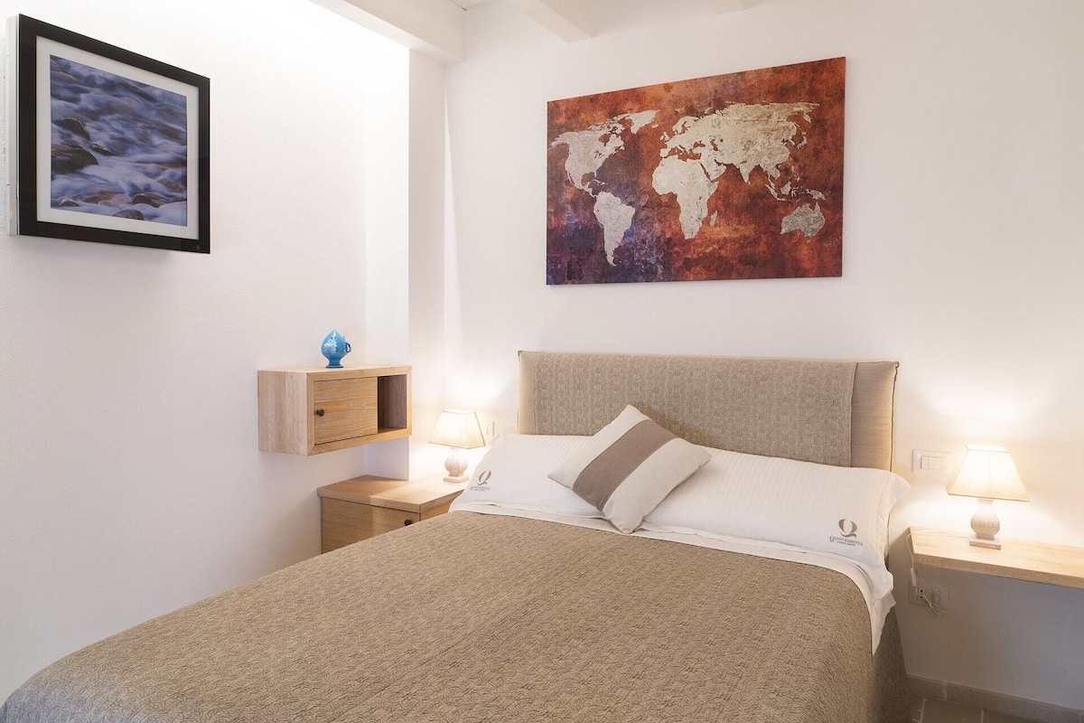 Een netjes ingerichte slaapkamer met een bed, twee nachtkastjes, een wereldkaart als kunstwerk, een ingelijste foto en een kleine blauwe vaas op een houten plank.
