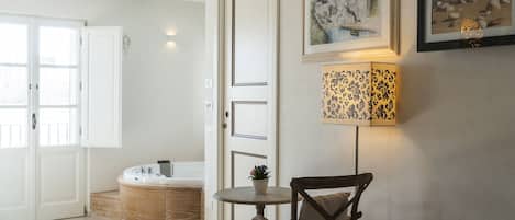 A room with a wooden cabinet, a round table with a chair, a wall-mounted lamp, and two framed pictures.