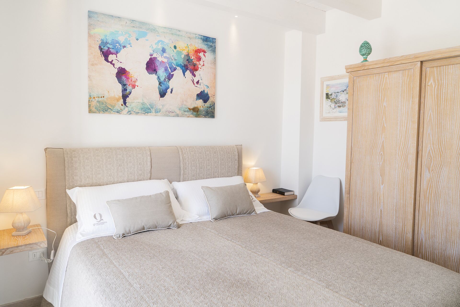Ein ordentlich eingerichtetes Schlafzimmer mit einem großen Bett, einem Holzschrank, einem Nachttisch mit Lampe und einem Wandbild einer Weltkarte.