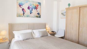 Una camera da letto ordinata con un letto grande, un armadio in legno, un comodino con una lampada e un quadro raffigurante una mappa del mondo.