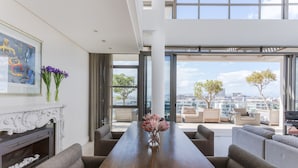 A modern living room with a fireplace, a dining table, and a view of the city through large windows. - Penthouse 702 Kylemore B (Stellenbosch)