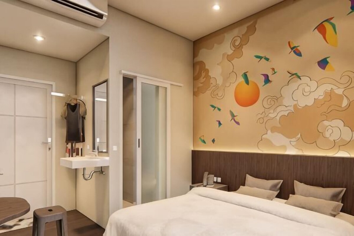 A hotel room with a bed, a vanity with a mirror, a sink, and a wall mural.