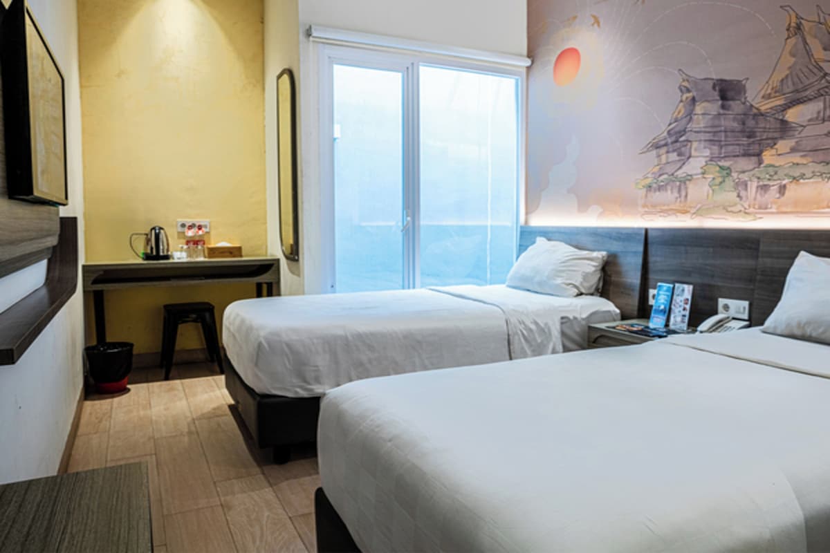 A hotel room with two beds, a desk, a chair, a window, and a wall with a mural.
