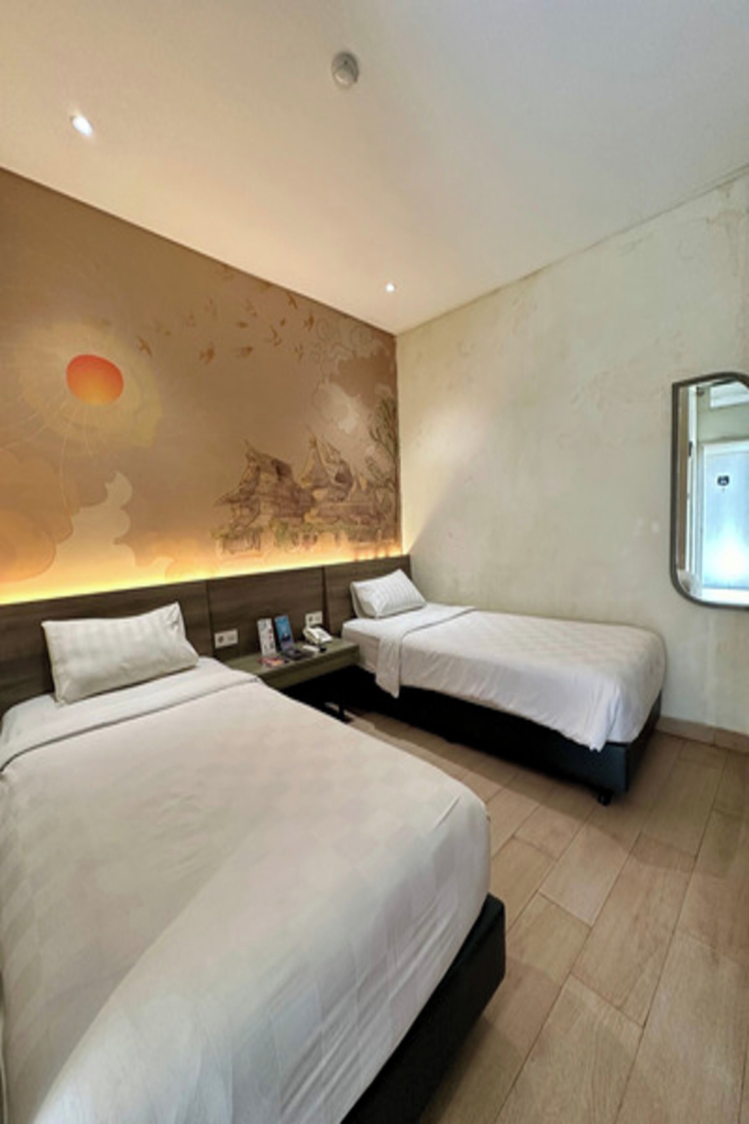 A hotel room with two beds, a nightstand, and a wall mural.