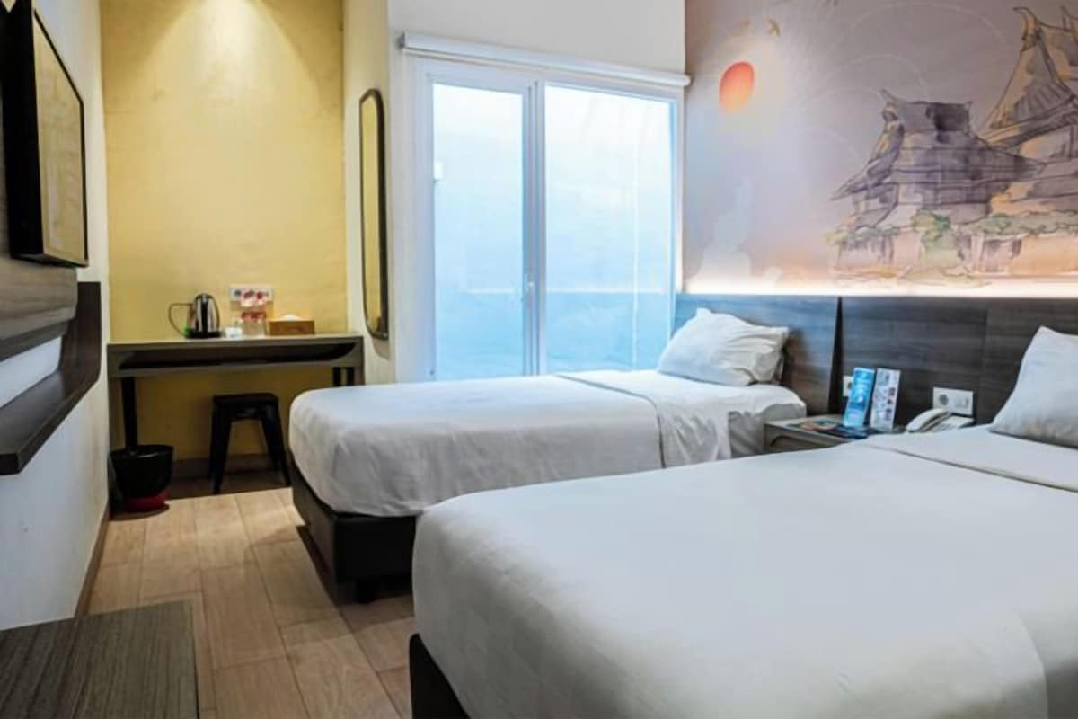 A hotel room with two beds, a desk, a chair, a window with a view, and a painting on the wall.