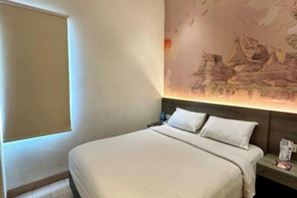 A hotel room with a bed, a nightstand, and a wall mural.