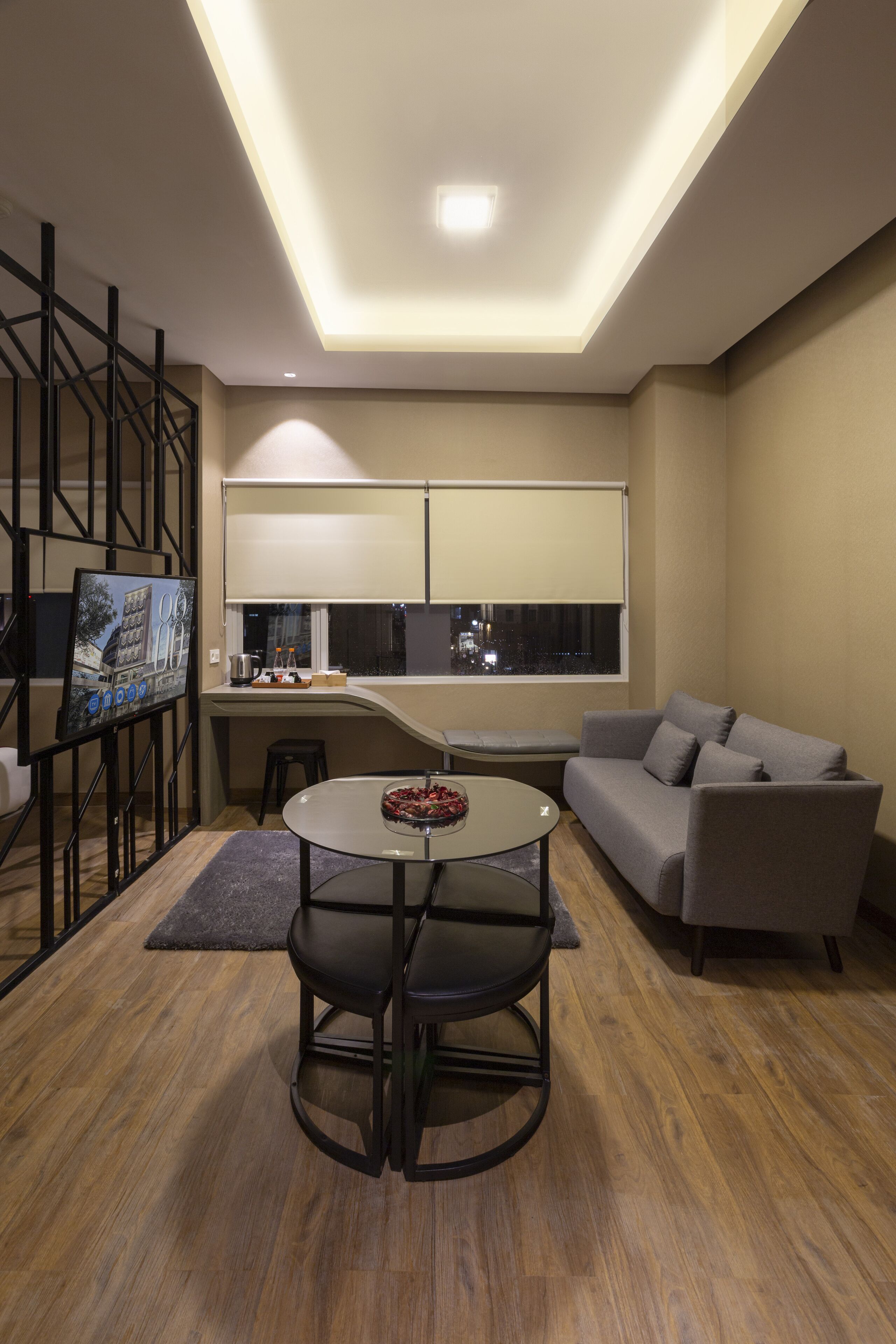 Un salon moderne comprenant un canapé, une table à manger avec des chaises, un téléviseur et une fenêtre avec des stores.