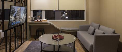Una sala de estar moderna con un sofá, una mesa de comedor con sillas, un televisor y una ventana con persianas.