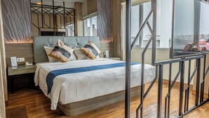 A modern hotel room with a large bed, a nightstand, a wooden floor, and a view of the city through large windows. - Hotel 88 Alun Alun (Bandung)