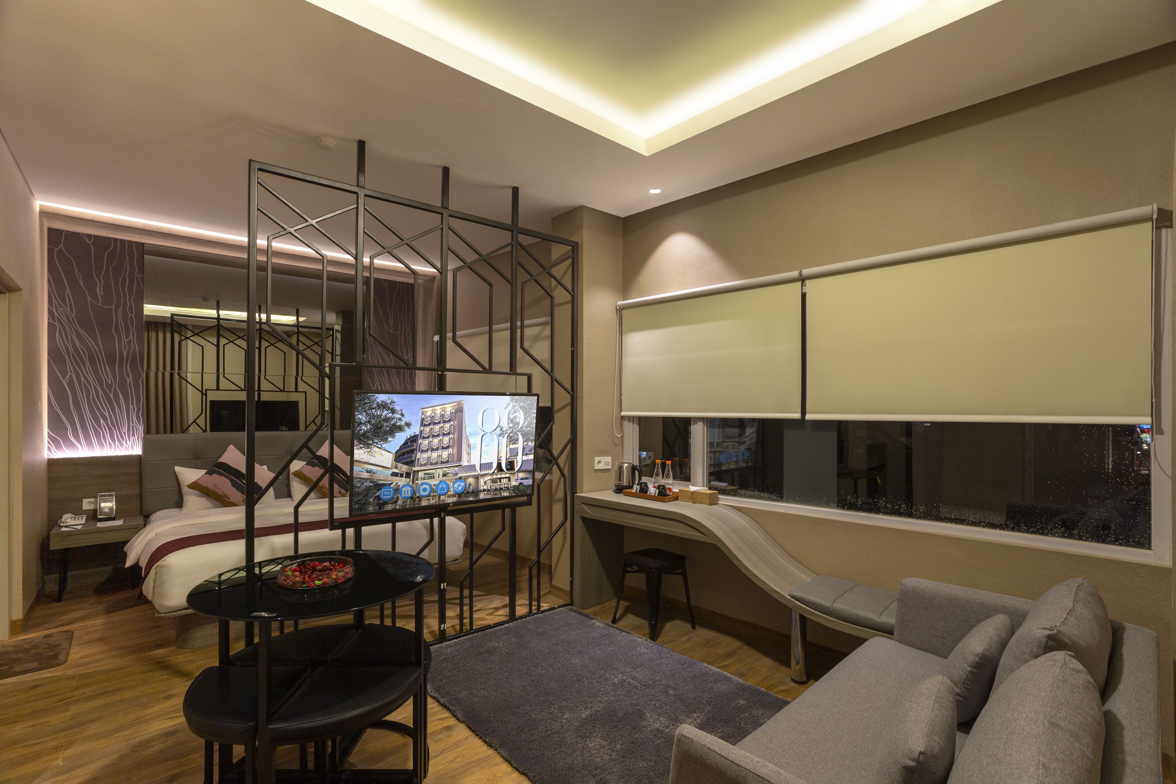 Una habitación de hotel moderna con cama, escritorio, televisor y un ventanal grande.