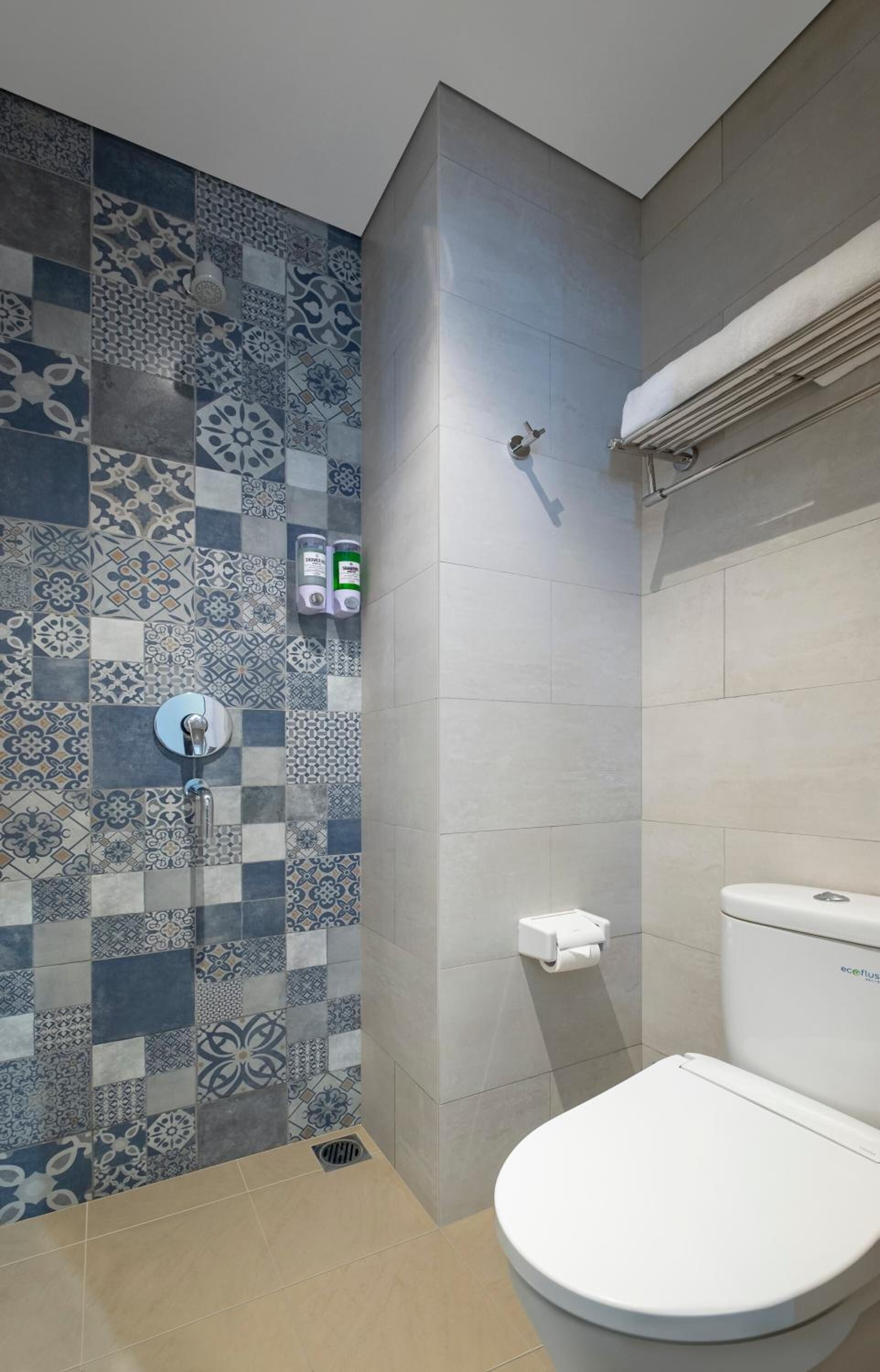Un baño con pared de ducha azulejada, un inodoro y un perchero para toallas.