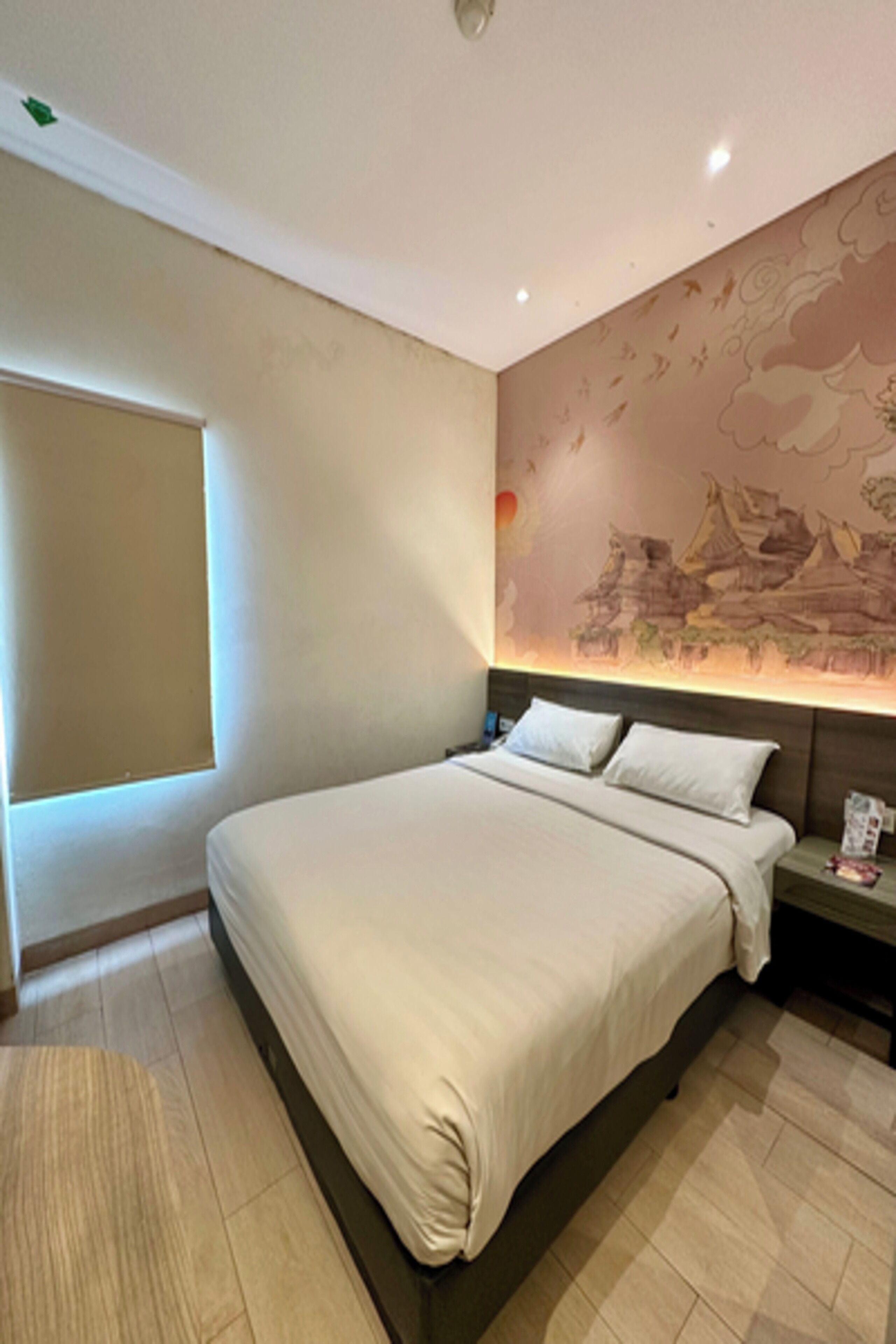 A modern hotel room with a large bed, a nightstand, and a wall mural.