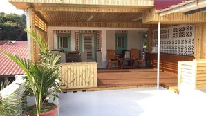 Un espace extérieur abrité doté d’un plancher en bois, d’un coin salon avec des chaises et d’une plante en pot.