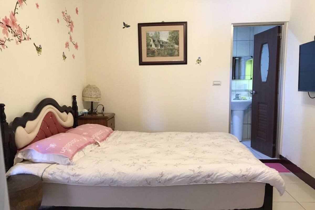 A bedroom with a bed, a nightstand, a lamp, a framed picture on the wall, and a door leading to a bathroom.