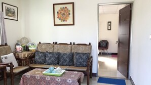Un salon comprenant un canapé, des fauteuils, une table basse et une table à manger. Une porte donne accès à une autre pièce.