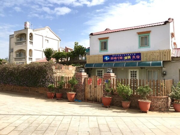 A building with a blue sign, a wooden fence, and potted plants.