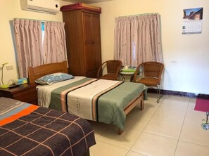 A hotel room with two beds, a wooden wardrobe, a chair, a small table, and a calendar on the wall.