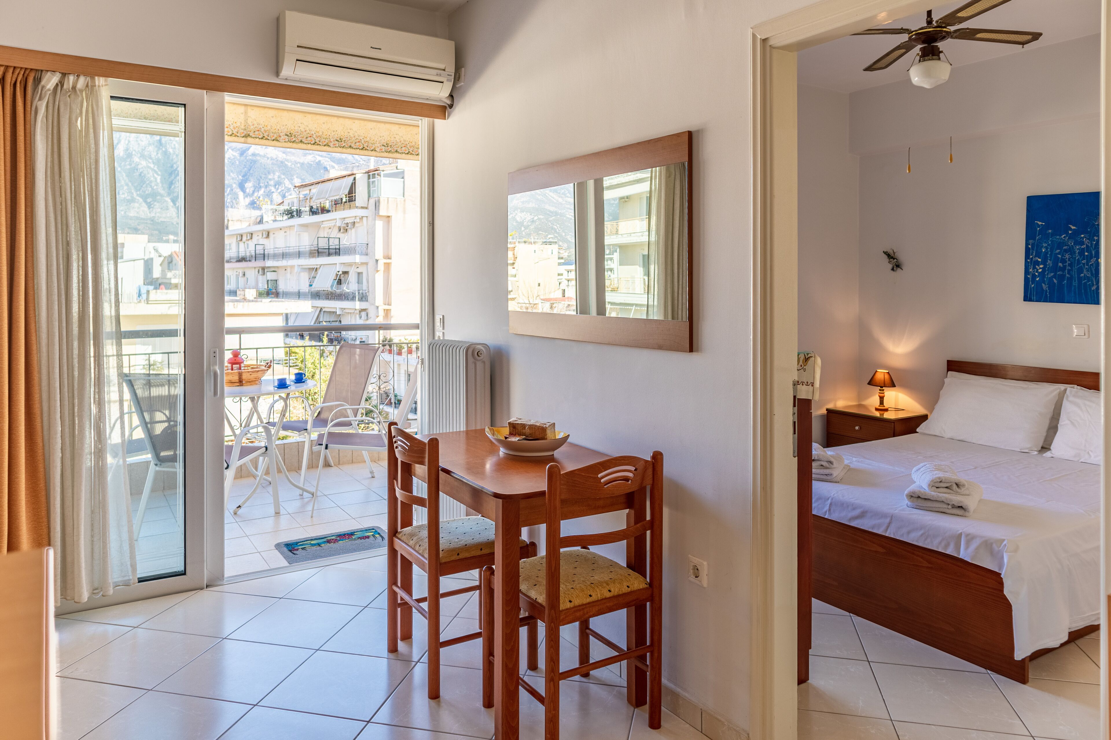 Una camera d'albergo con un letto, un tavolo con sedie, un balcone vista edifici e un condizionatore d'aria.
