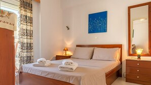 Ein ordentlich eingerichtetes Schlafzimmer mit einem hölzernen Bett, zwei Nachttischen mit Lampen, einem an der Wand befestigten Spiegel und einem blauen Kunstwerk über dem Bett.