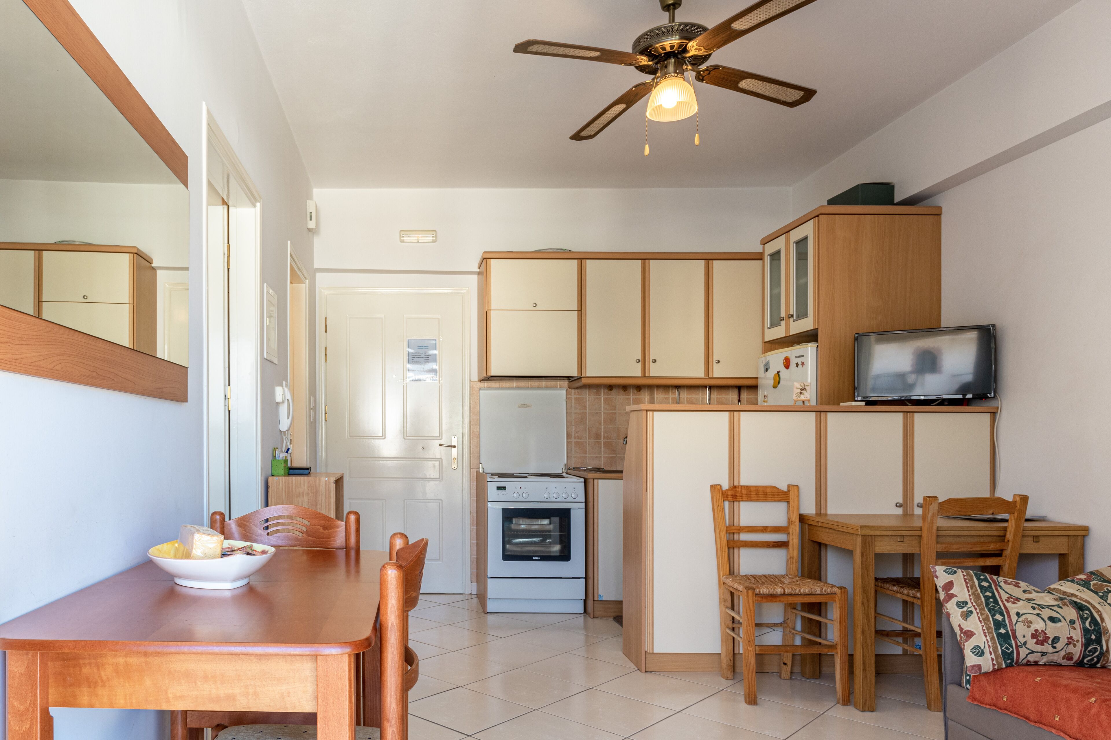 A compact kitchen with wooden cabinets, a built-in oven, a refrigerator, and a dining area with a table and chairs.